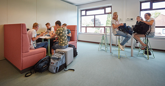 Leerlingen werken samen aan hoge Trigon tafels en vooraan zitten ze op de MC Sofa aan de Club tafel.