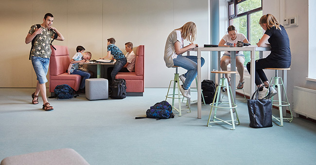 Leerlingen werken samen aan hoge Trigon tafels. Verderop zitten ze op de MC Sofa aan de Club tafel.